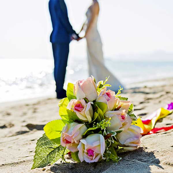 Bridal bouquet on beach with couple in the background