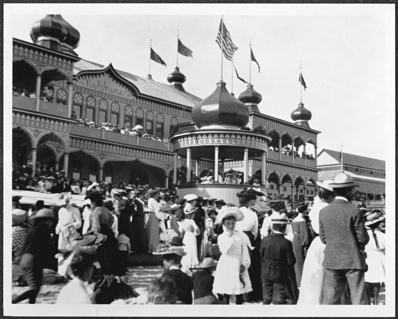 On the beach outside the Neptune Casino, the ladies of Omega Nu sorority (seated in the bandstand) and the crowd watch the end of a sack race in 1904.